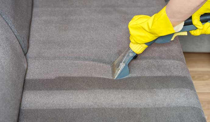 A person is cleaning a sofa with equipment