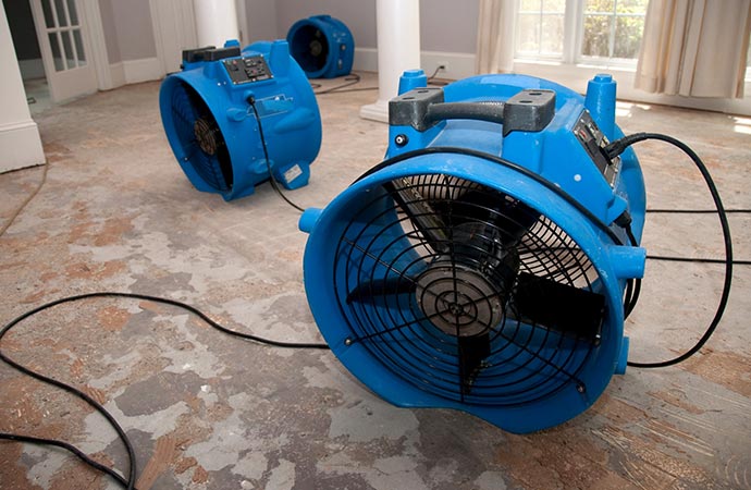 Three industrial fans are drying a damaged concrete floor.