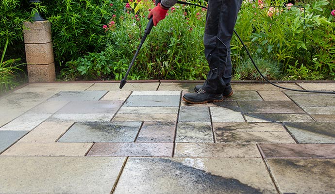 a person cleaning brick paver uisng a pressure washing tool