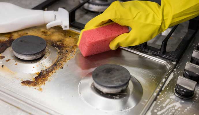 a person wearing a yellow gloves cleaning grease stains around the burners