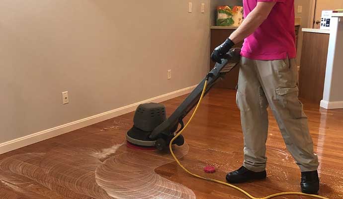 A person is cleaning wooden floor with a cleaning machine